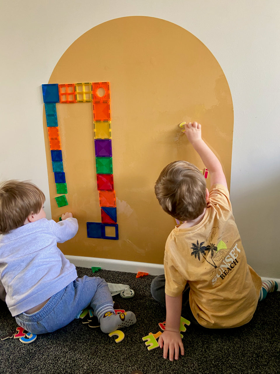 Two Children playing with magnetic tiles on a magnetic wall decal