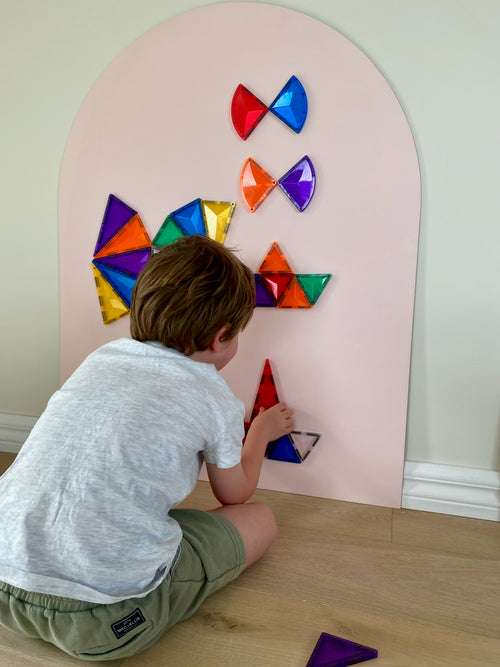 Child playing with colorful geometric shapes on a pink wall decal
