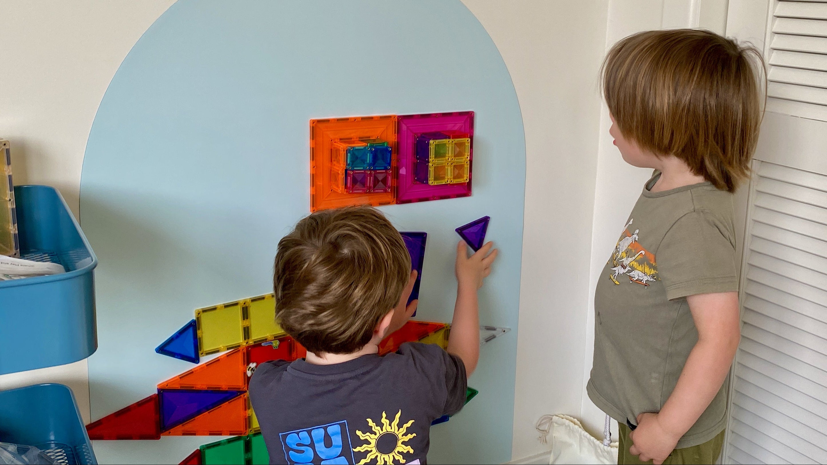 Two children playing with colorful geometric shapes on a wall.